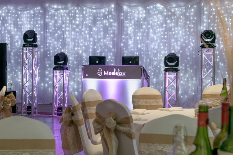Wedding DJ setup with pink venue uplighting. A starlit backdrop lights up the background at a beautifully decorated wedding reception.