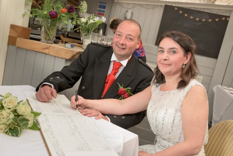 Newlywed couple signing the registry. Wedding flowers decorate the background.
