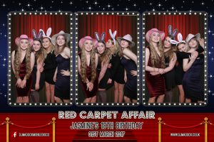 Picture taken by photo booth mirror. A red carpet birthday party theme. Young friends are posing for a selfie at a 21st birthday party.