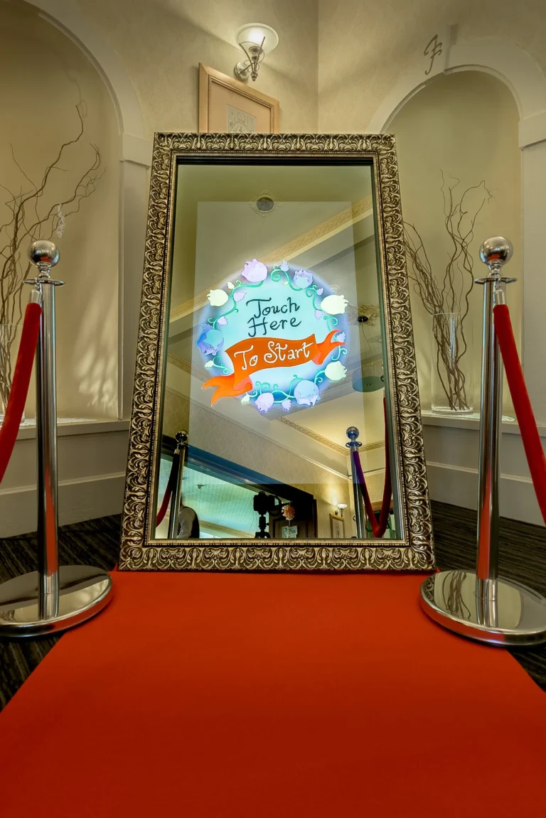 Red carpet and rope barriers lead to way to photo booth selfie mirror at a wedding reception.