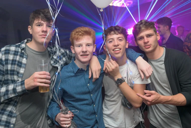 Young men posing for camera at birthday party disco. Balloons and light show with laser in the background.