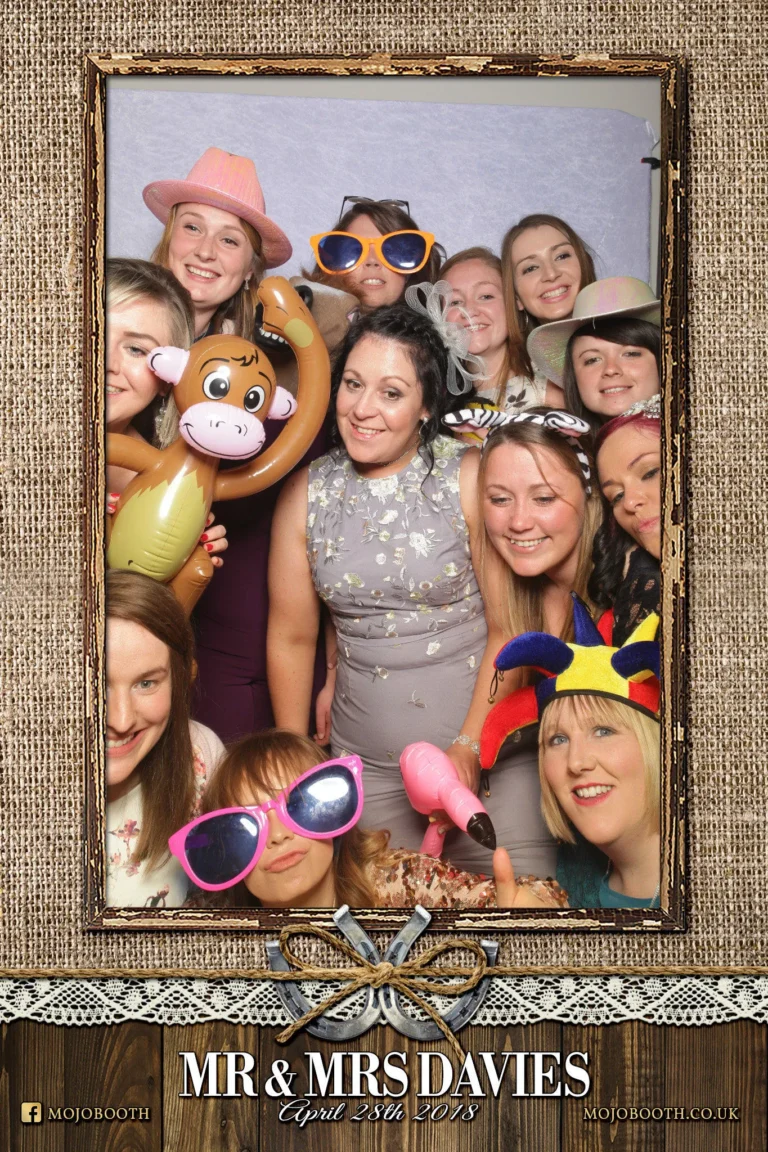 Picture taken by photo booth mirror encapsulated in rustic wood and burlap template. A large group of wedding guests squeeze together for a selfie.