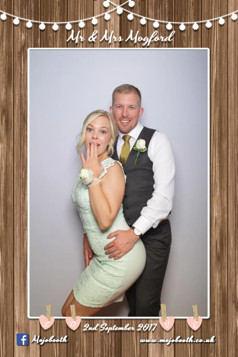 Picture taken by photo booth mirror encapsulated in a wood and string lights template. The bride and groom pose for their wedding photo.