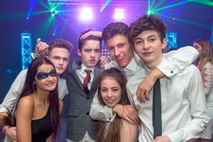 High school students pose for photo at promenade dance. Mobile disco DJ is in the background.