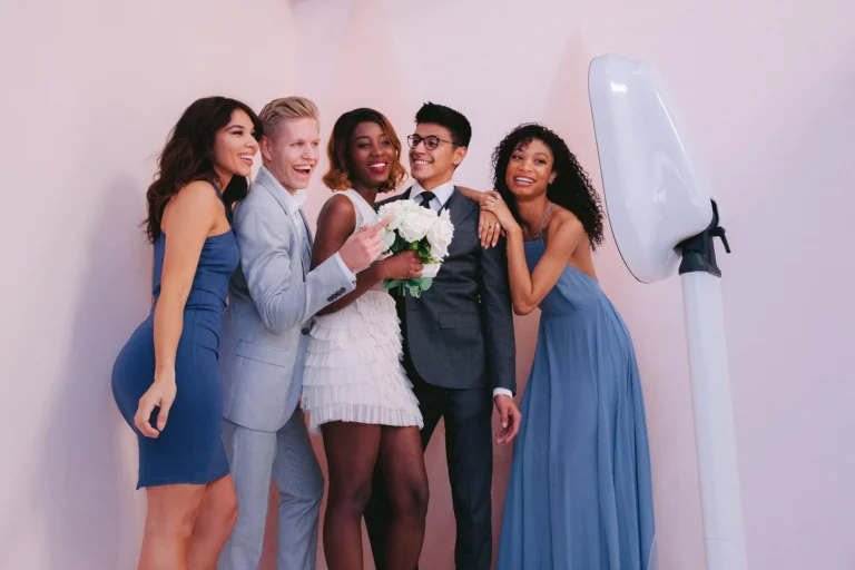 A group of friends are taking a picture using the Salsa photo booth pod at a wedding reception. Pink venue uplighting reflects on the walls.