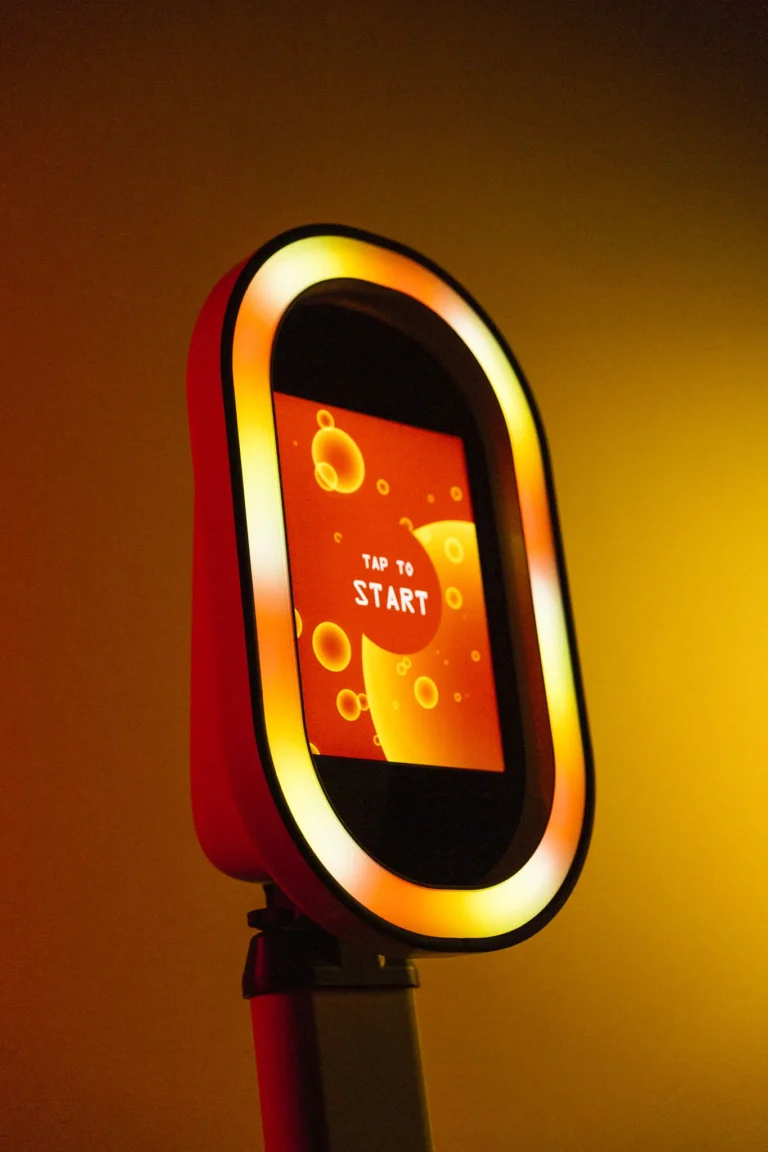 Salsa photo booth pod displays orange and yellow light. Venue uplighting illuminates the background with an orange glow.
